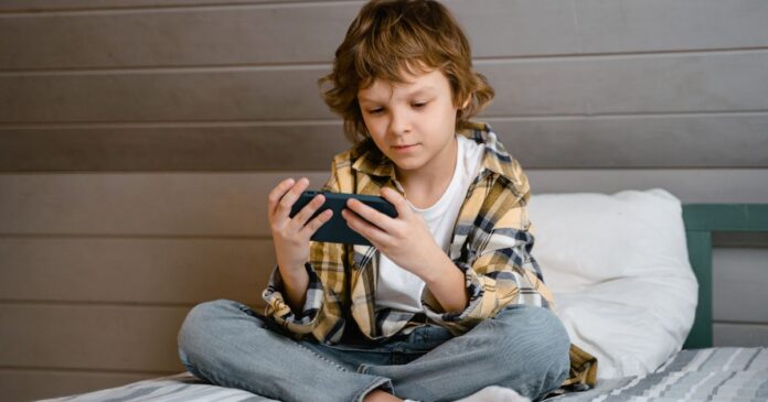 child sitting on bed looking at phone